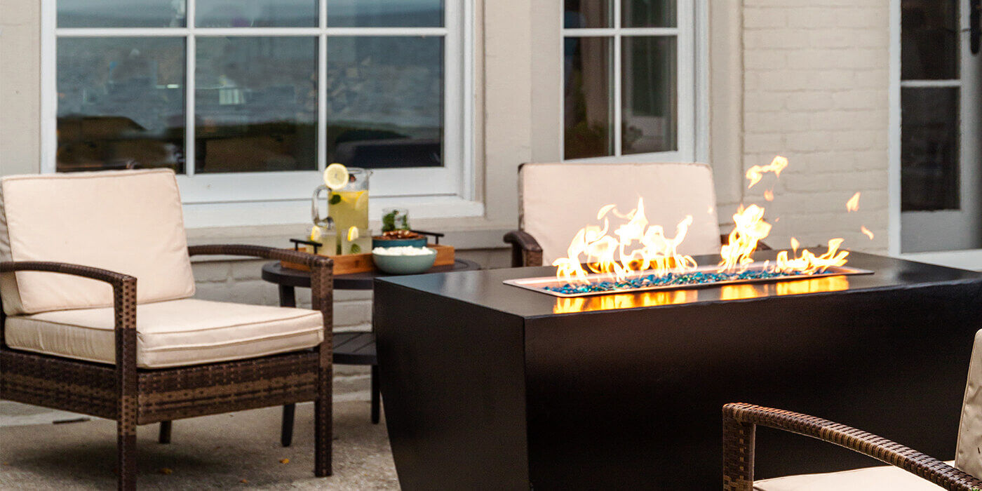 An outdoor living space with wooden patio furniture and a steel gas fire pit