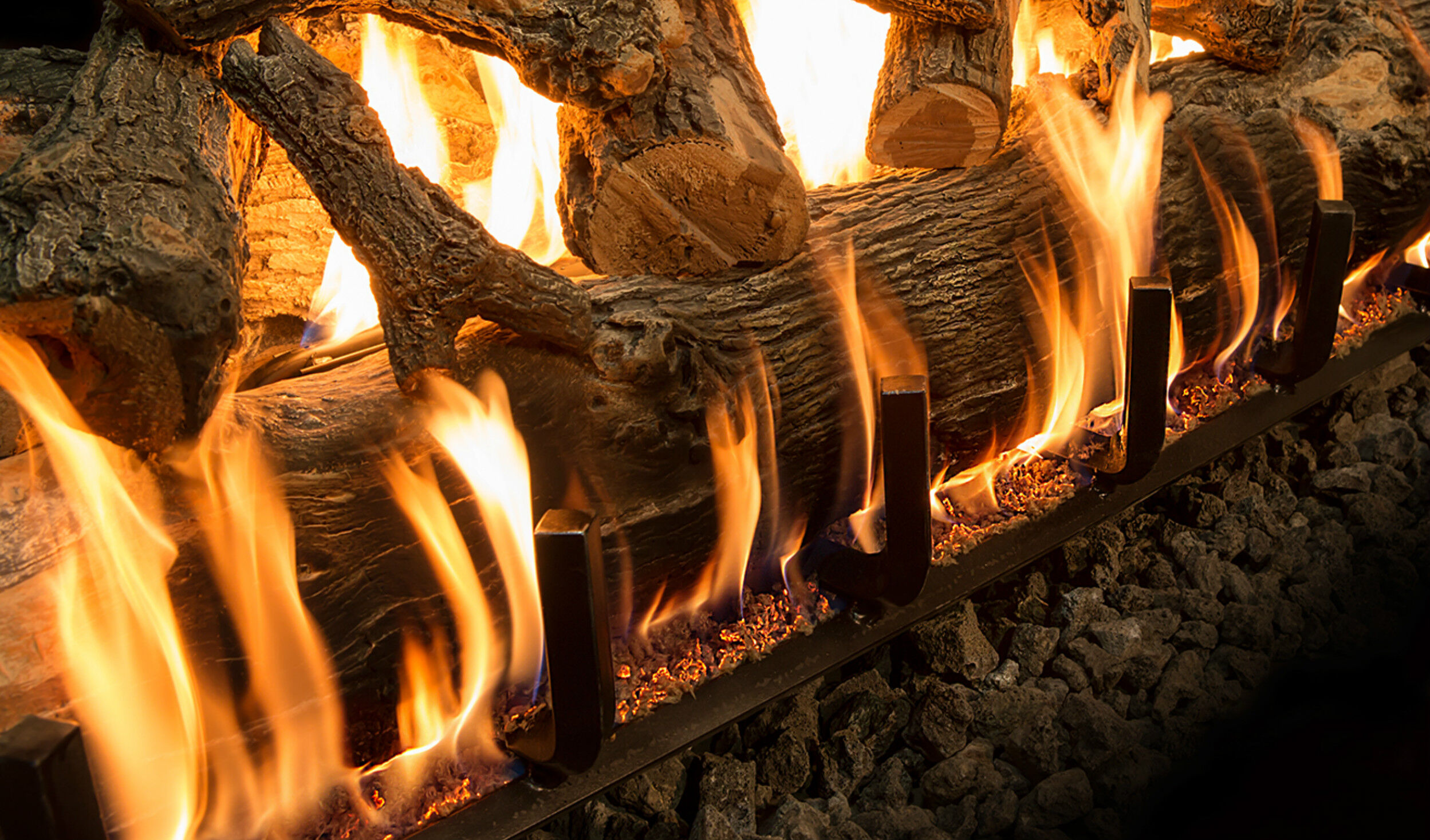A close-up view of a rustic gas log set with hand-painted bark details and orange flames.