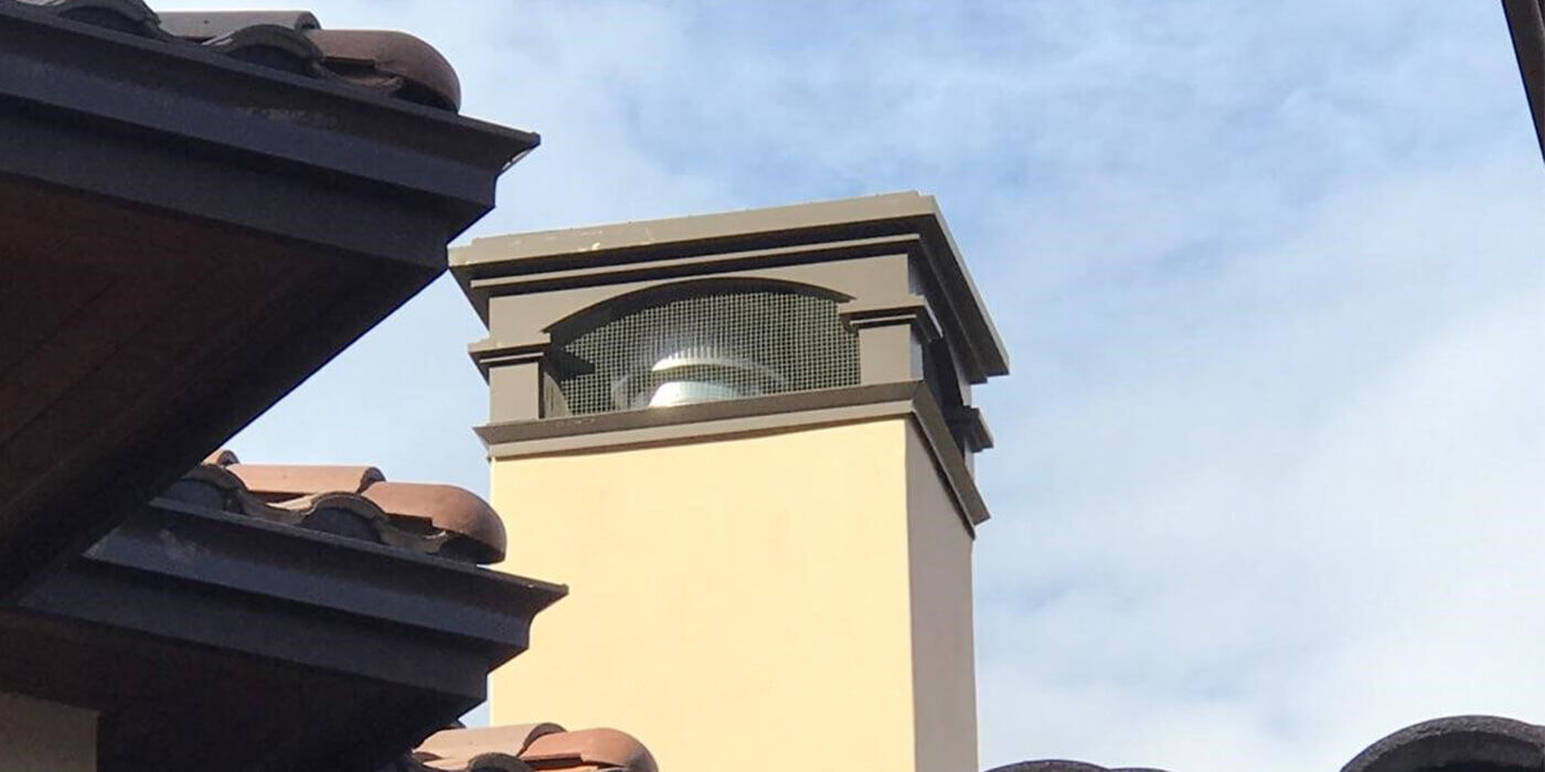 A masonry chimney with a stainless steel chimney cap and decorative shroud