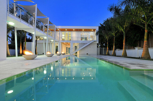 Five gas fire bowls next to a swimming pool in an ultramodern outdoor patio