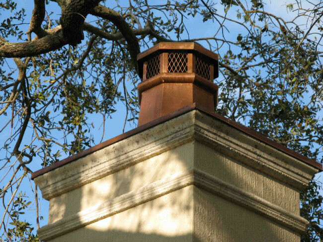 Copper chimney cap on a masonry chimney with trees hanging overhead