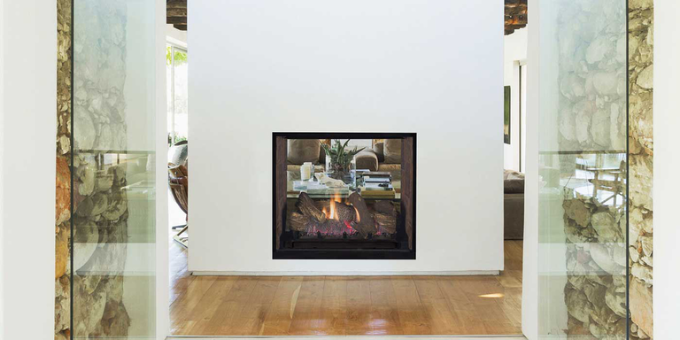 An modern entryway with a large partition and a see-through gas fireplace with a rustic gas log set