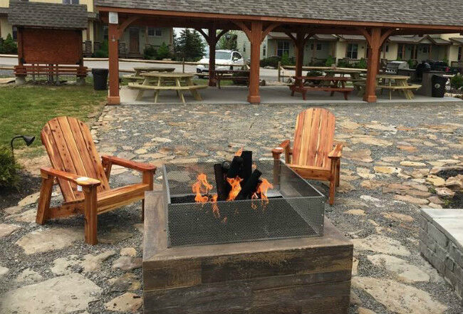 Outdoor stone patio with a square fire pit and two adirondack chairs in front of a pavillion