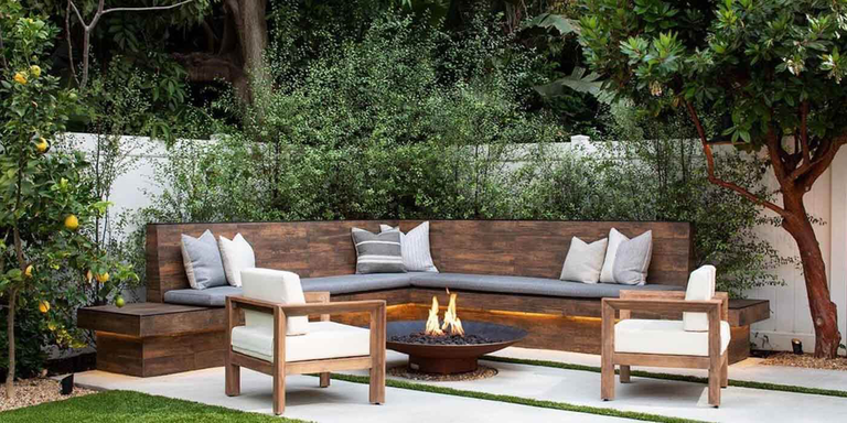A custom-built seating and fire pit area in a contemporary backyard with a wall of lush greenery and a metal gas fire bowl with an aged patina finish