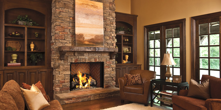 A rustic living room with a large, square wood burning fireplace and a natural stone hearth