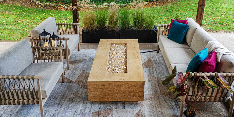 The FlameCraft Tuscan gas fire pit on a wooden outdoor deck with a patio furniture set that includes a sofa and two chairs