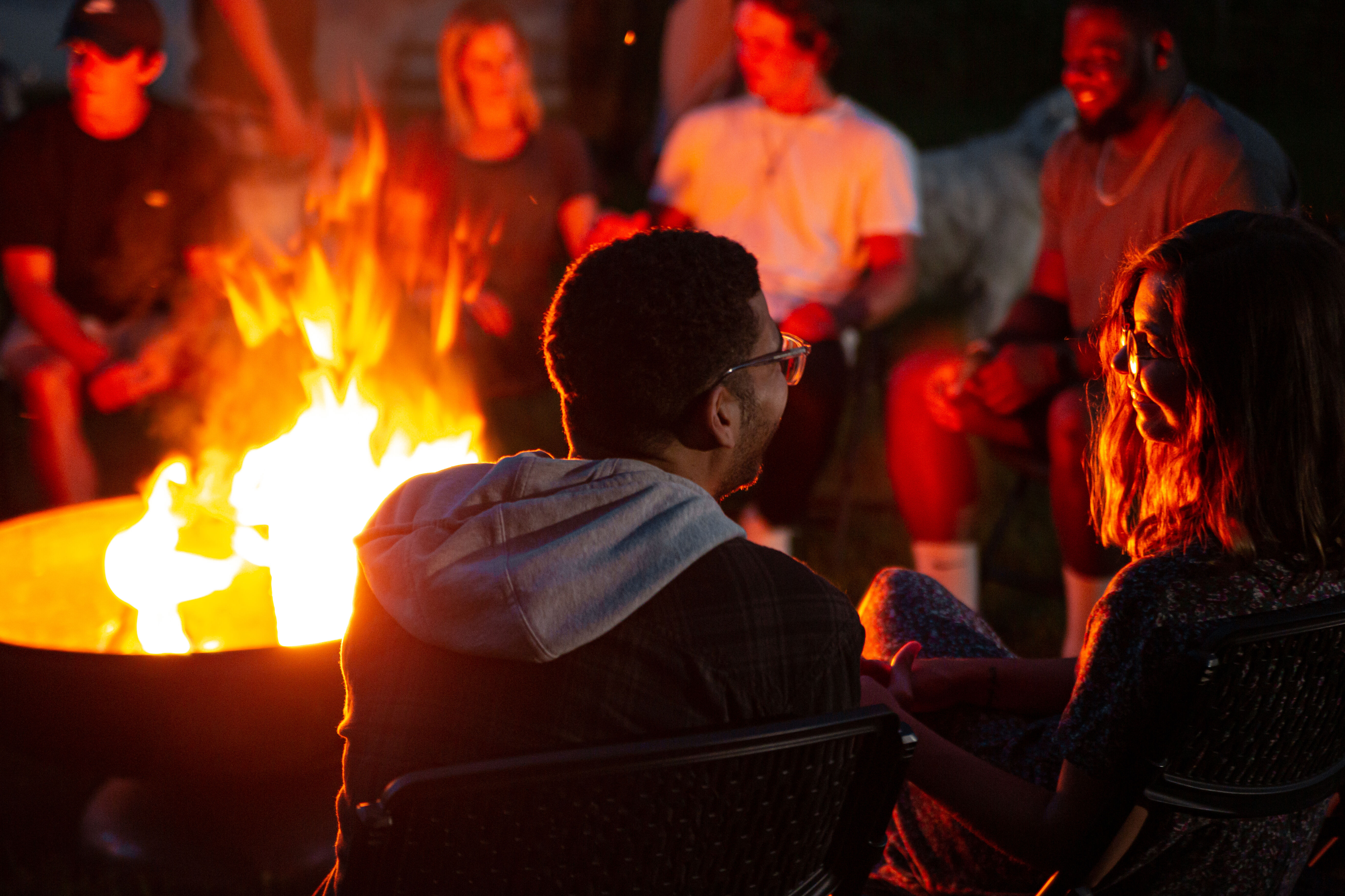 A group of friends gathering around a wood burning fire in the backyard.