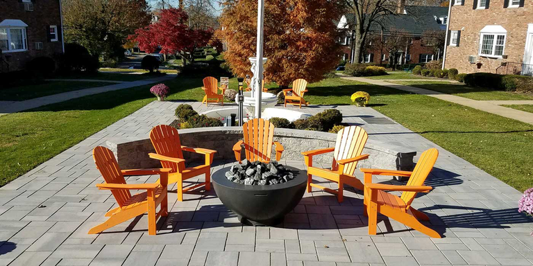 A public outdoor patio space with four chairs and a gas fire bowl in the center