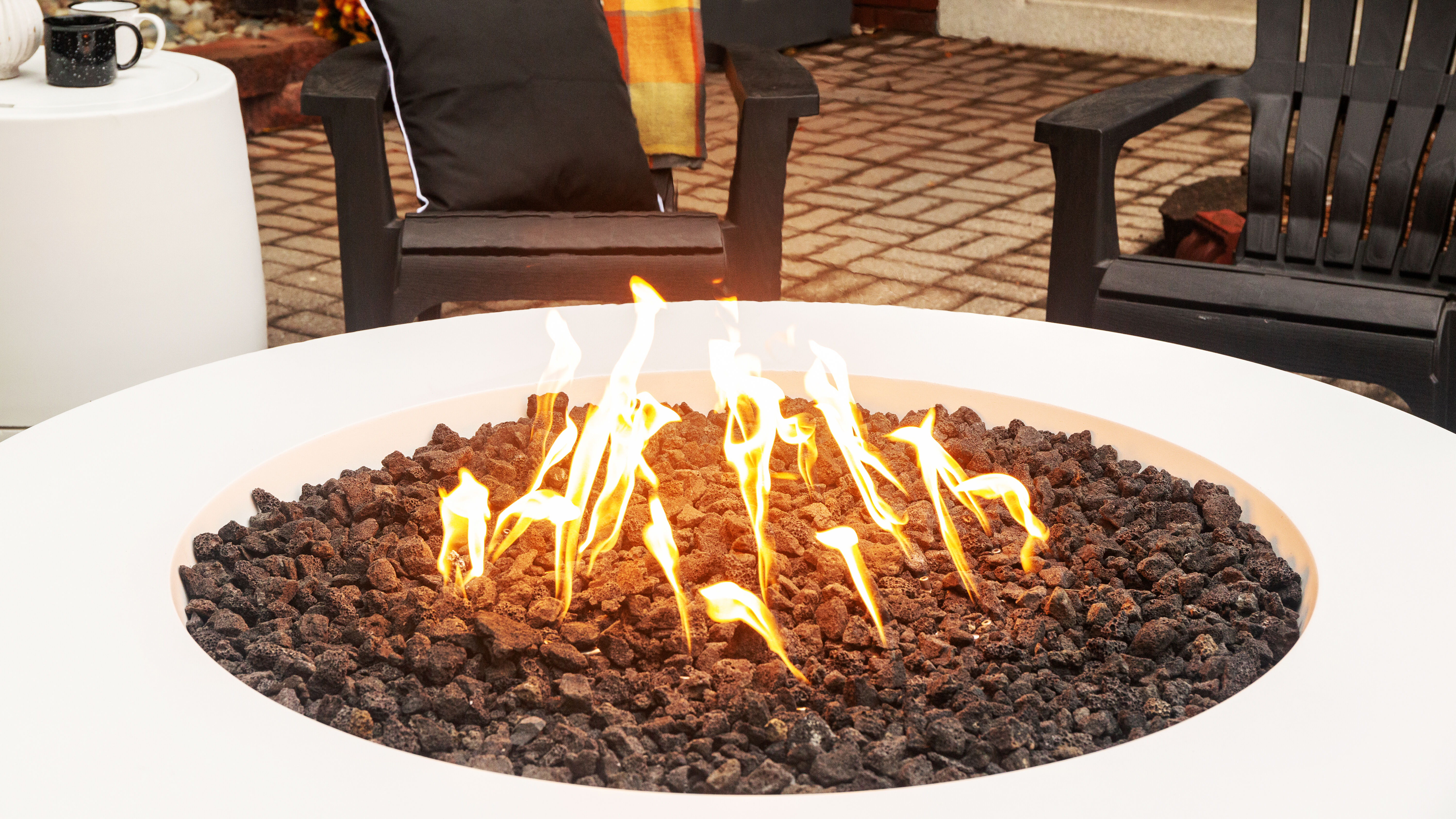 A close-up view of a white, 36-inch Tondo gas fire pit from FlameCraft with black lava rock media and an HPC gas fire pit burner.