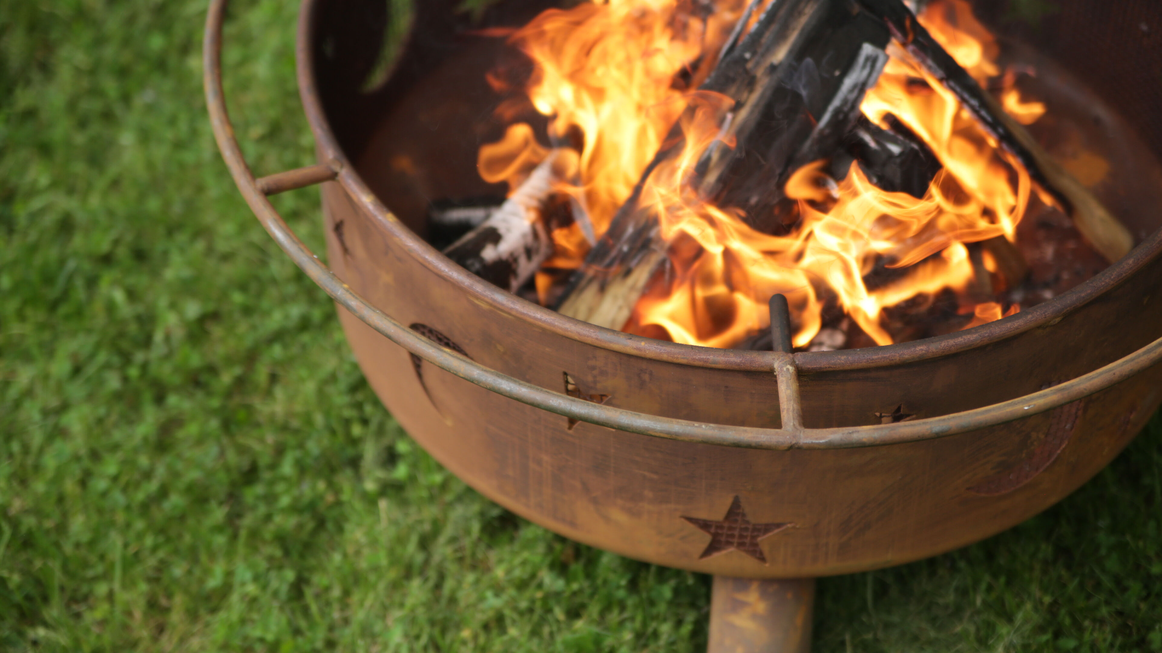 A close-up of a steel wood burning fire pit burning in a backyard.