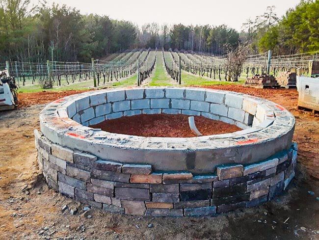 Unfinished masonry fire pit in front of a vineyard