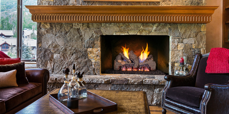 A traditional living room with a stone hearth, wooden mantel, and traditional square fireplace with a rustic log set that resembles real firewood