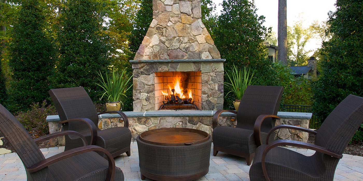 An outdoor patio space with four chairs, a fire pit, and a large stone outdoor gas fireplace with a chimney stack.