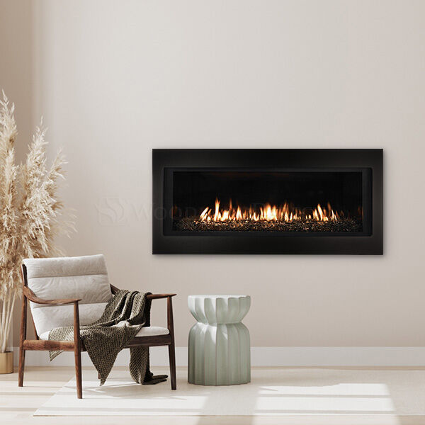 A minimalist living room with a single chair, a ceramic white stool, a neutral-colored plant in the corner, and a black, linear fireplace with yellow flames and glowing embers.