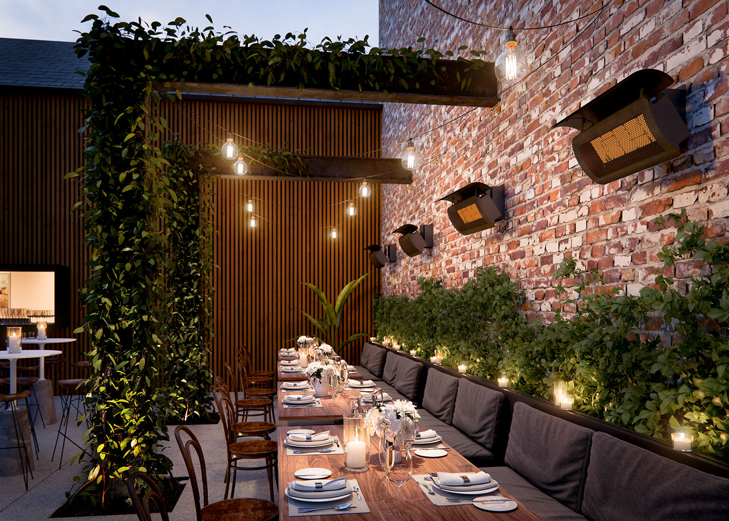 An outdoor restaurant patio with a long table and multiple black chairs, an exposed-brick wall with vines, and four gas patio heaters hung around the top of the wall.