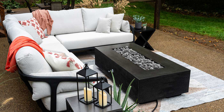 An outdoor patio space with a white sectional couch and a black Zen Gas Fire Pit by FlameCraft made of durable, glass fiber reinforced concrete
