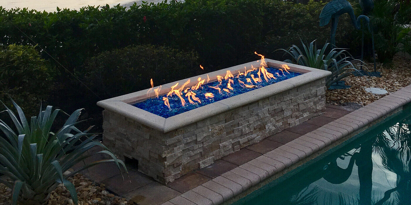 A natural stone linear gas fire pit with bright blue fire glass media 