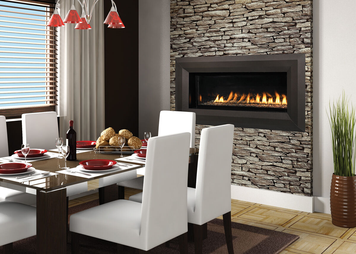 A contemporary dining room with a glass dining table, six white fabric chairs, an orange glass lighting fixture, a floor plant, and a large natural stone feature wall with a linear gas fireplace.