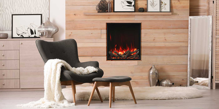 A minimalist living room with light wood-plank finished walls, light natural wood furniture and shelves, a gray accent chair with a white blanket, a floor mirror, and a slim, vertical electric fireplace.