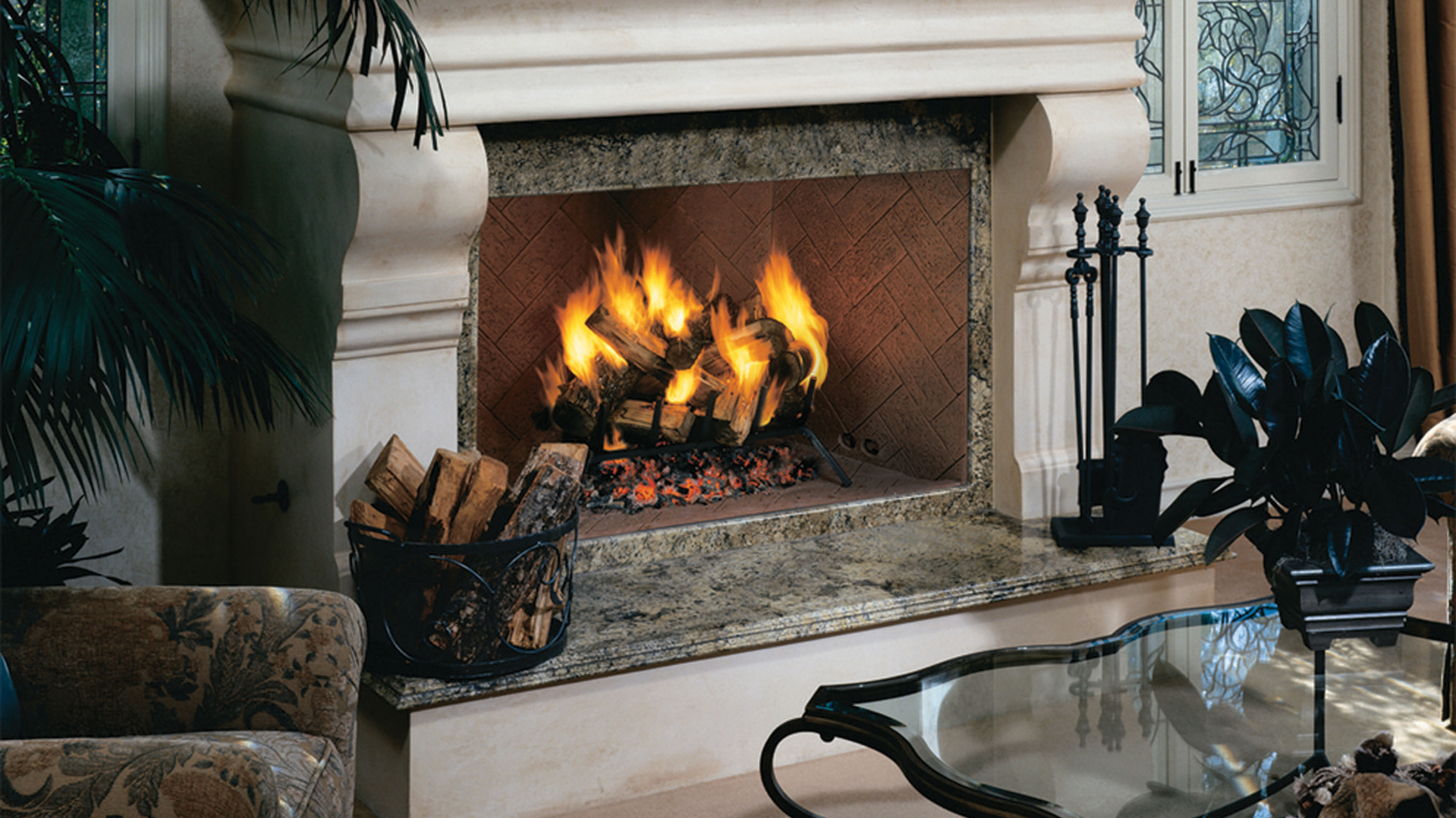 A traditional hearth with a large white, decorative mantel, a marble hearth platform, a square wood burning fireplace, and a set of black fireplace tools.