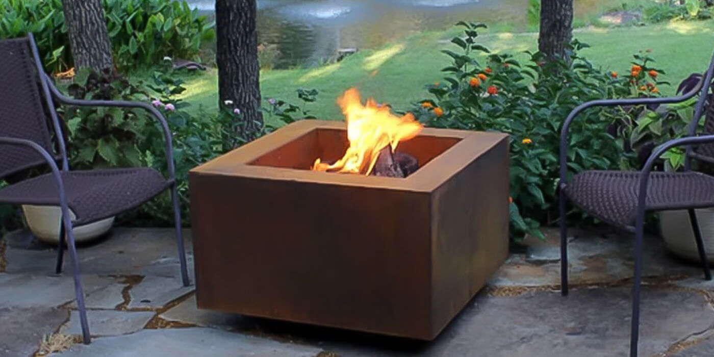 A square shaped wood burning fire table set up outside on a patio in the center of a seating area