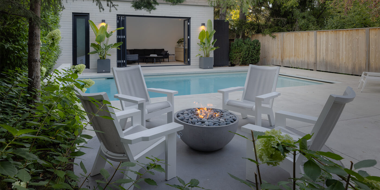 An outdoor sitting area near a with four chairs and a small gas fire bowl with a round fire pit burner