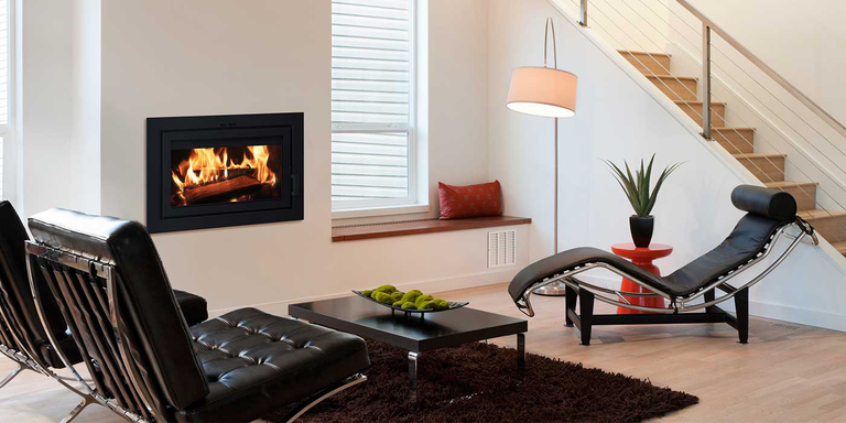 A modern living room with black leather chairs and a fireplace that has been converted with a wood stove insert.