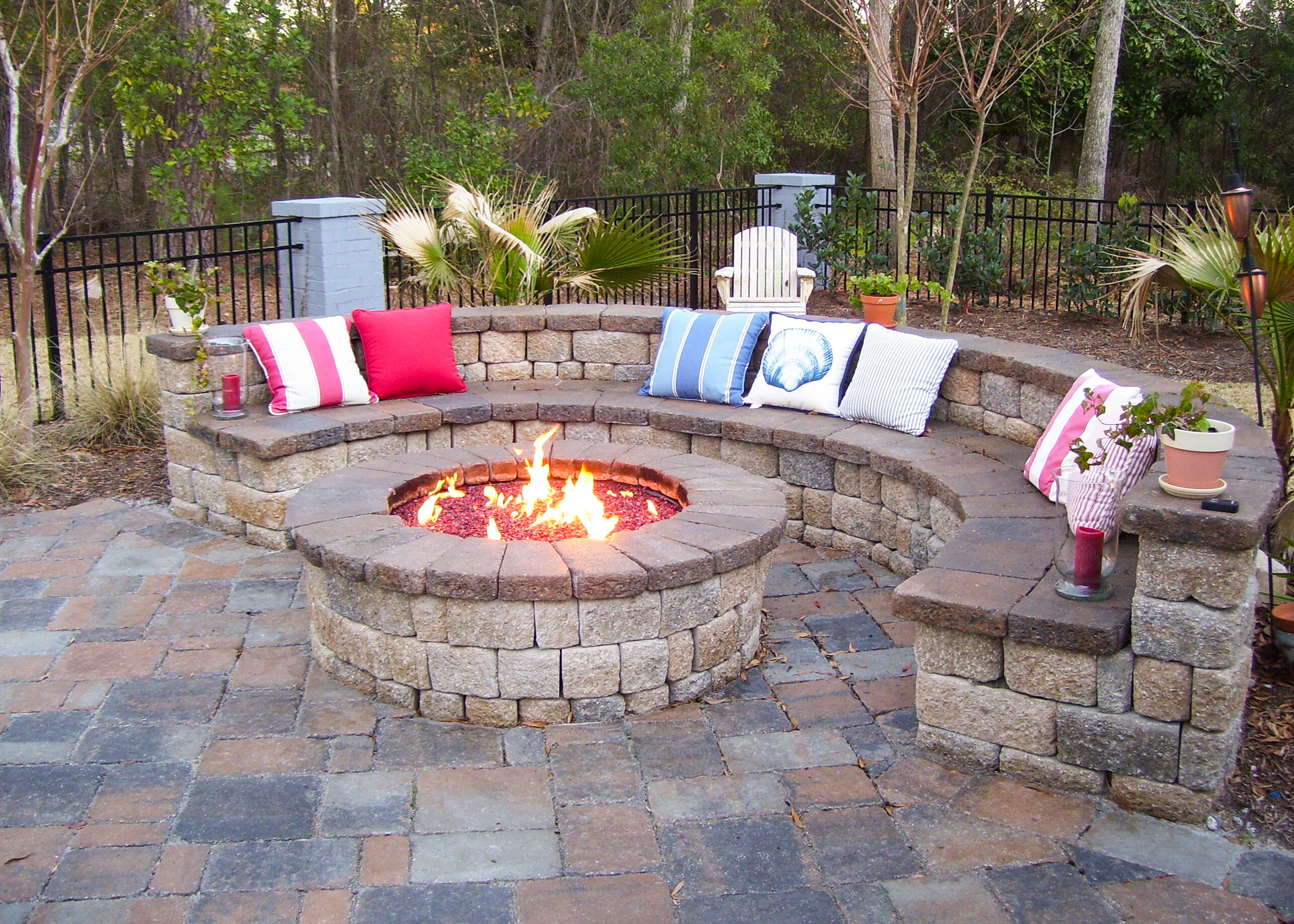 An outdoor lounge space made of brick pavers and a large, round fire pit built with matching brick pavers and topped off fire glass media.