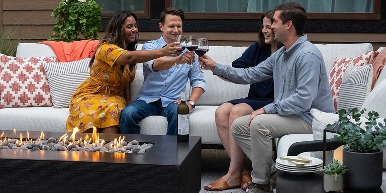 Two couples sitting around a FlameCraft Zen Gas Fire Pit, clicking their wine glasses together in celebration.