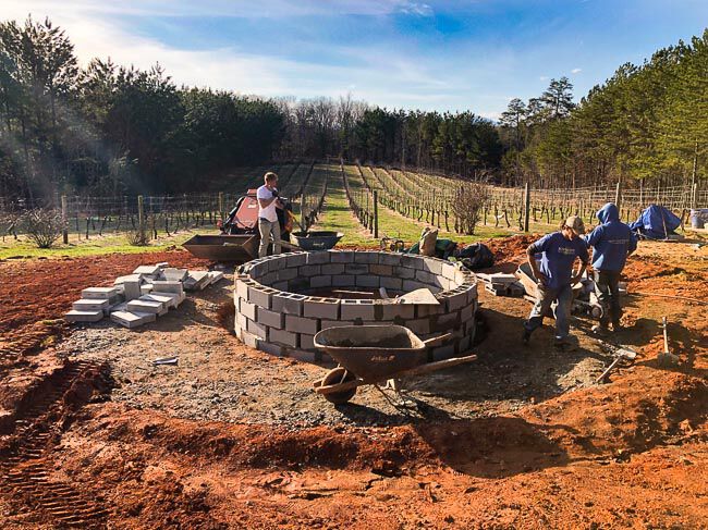 Workers building a fire pit frame in front of a vineyard