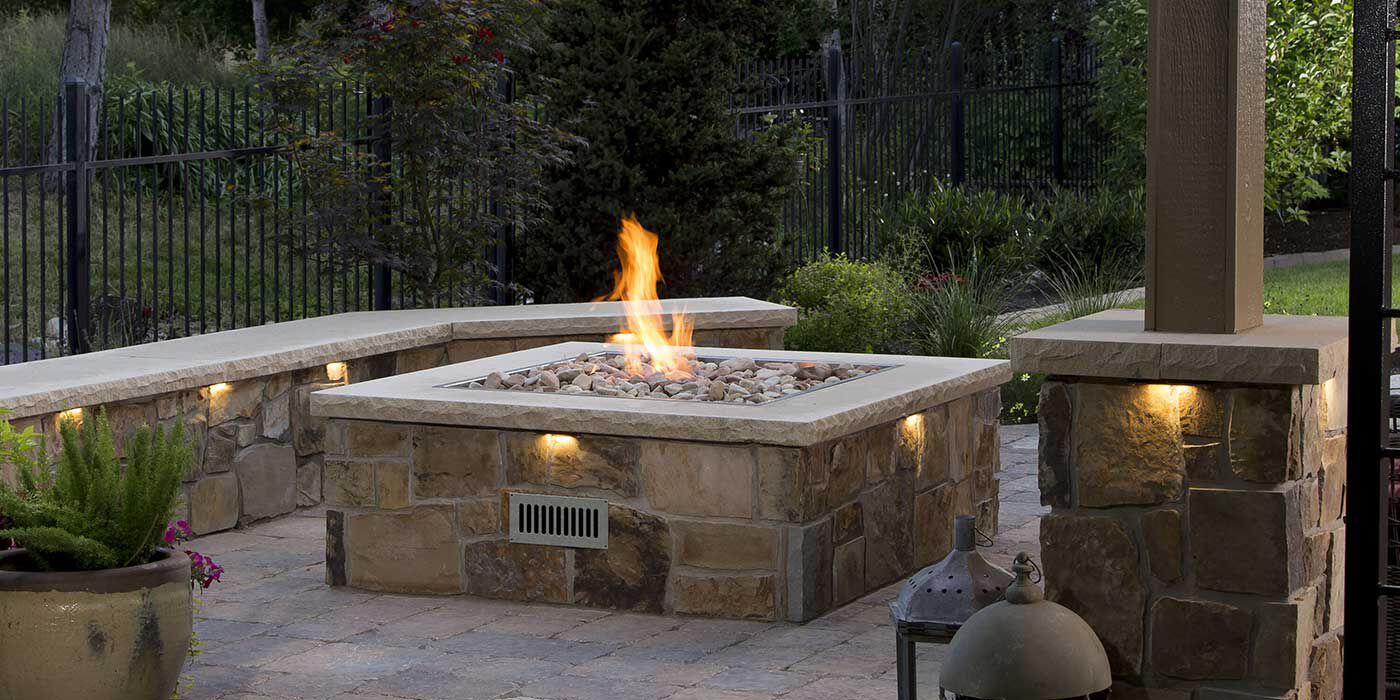 A large, square custom-built gas fire pit made of natural stone and concrete