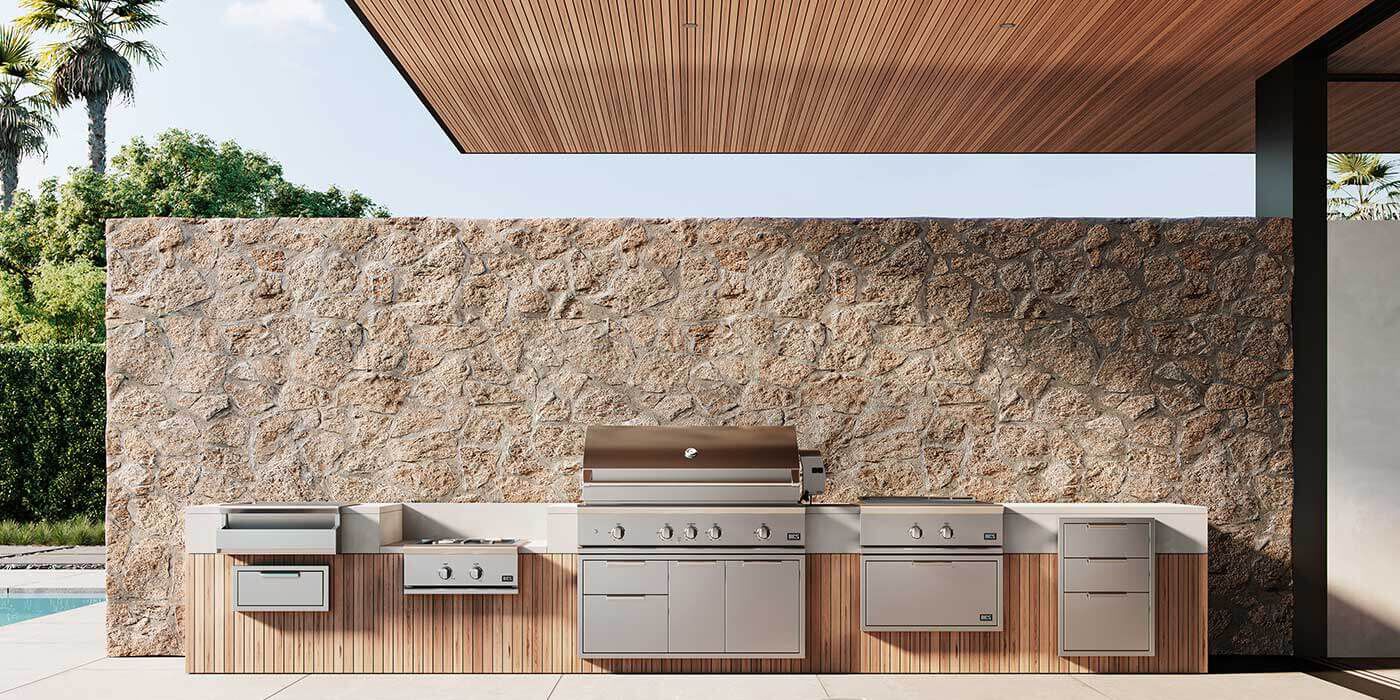 A large outdoor kitchen island with a built-in stainless steel grill and matching drawers, doors, and refridgerator.