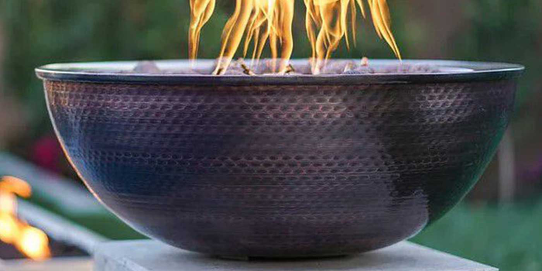 A close-up of a copper gas fire pit installed next to a pool
