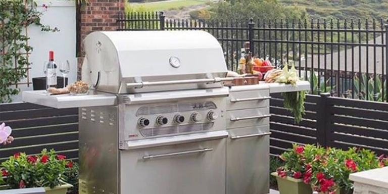 A gas grill mounted on a cart with side shelves and storage drawers