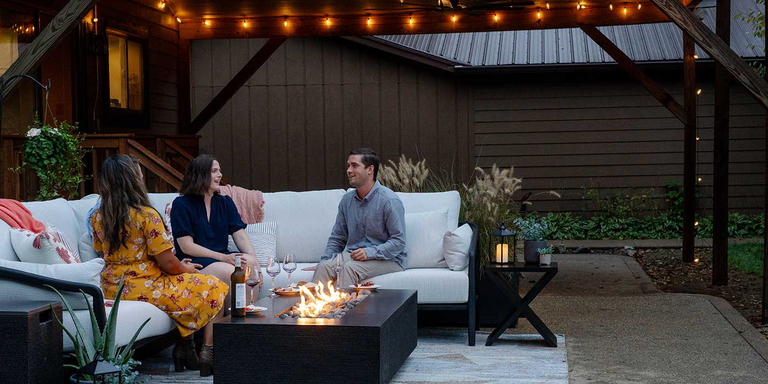 Four people sitting outside on a white sectional sofa with a FlameCraft Zen Gas Fire Pit