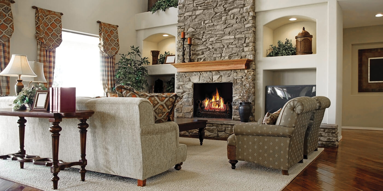 A cozy, traditional living space with a stone hearth, wood mantel, square fireplace, and massive gas log set with robust, natural flames.