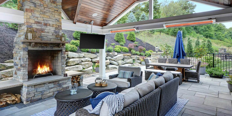 An outdoor living room with a large seating area and fireplace, a dining area, and two mounted patio heaters