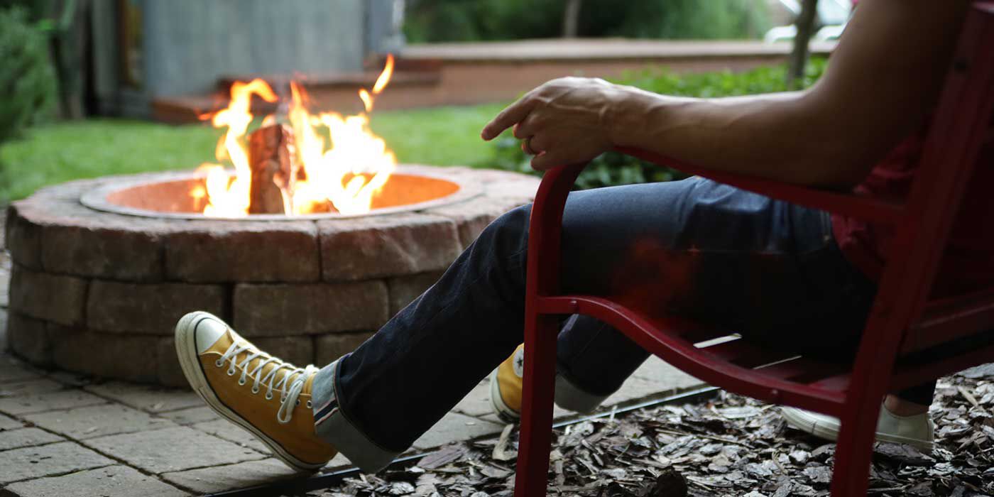 A person sitting next to a wood burning fire in the backyard.