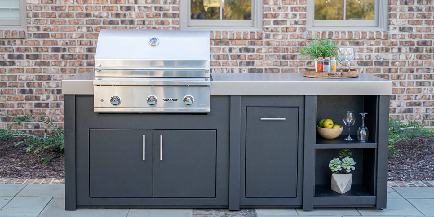 A small outdoor kitchen island with a stainless steel grill head, a refrigerator, and built-in storage doors and drawers.