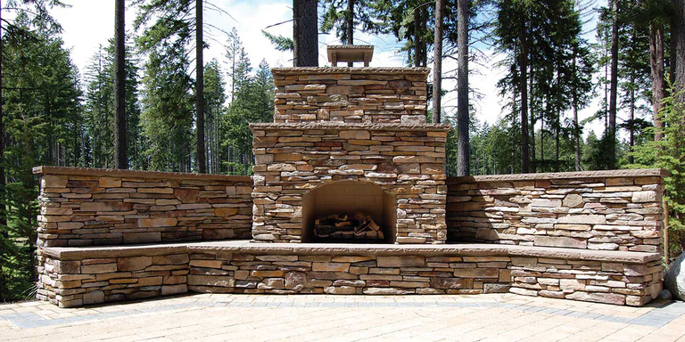An extra-large Standard Isokern outdoor fireplace finished with natural stone and a built-in limestone mantel and shelf.