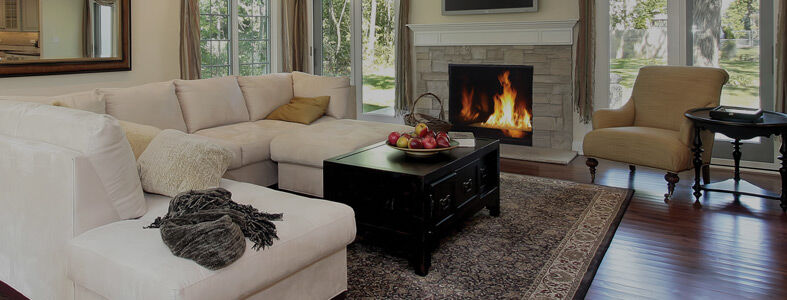 A traditional living room with a large white L-shaped couch, a beige accent chair, a black coffee table, and a brick hearth with a mantel and a square Superior fireplace.