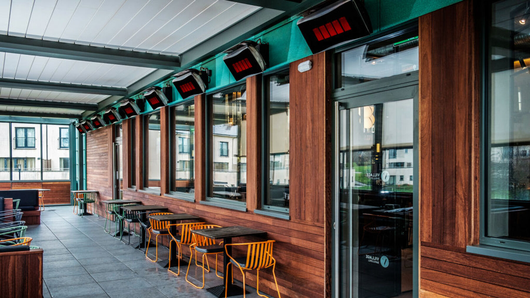 An outdoor restaurant patio space with multiple gas patio heaters mounted along the upper walls.