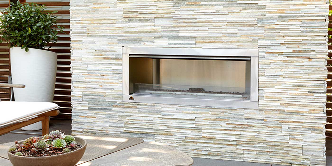 A custom outdoor feature wall with a natural stacked stone finish and a stainless steel, linear outdoor gas fireplace.