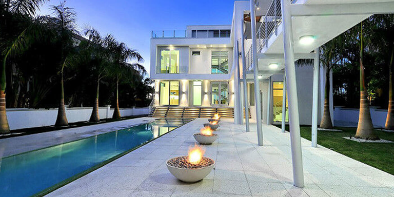 Stone patio with five gas fire bowls next to a swimming pool at an ultramodern luxury home
