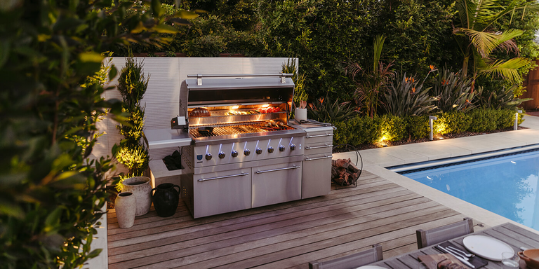 A large, cart-mounted stainless steel grill from American Made Grills, placed on an outdoor deck near a pool