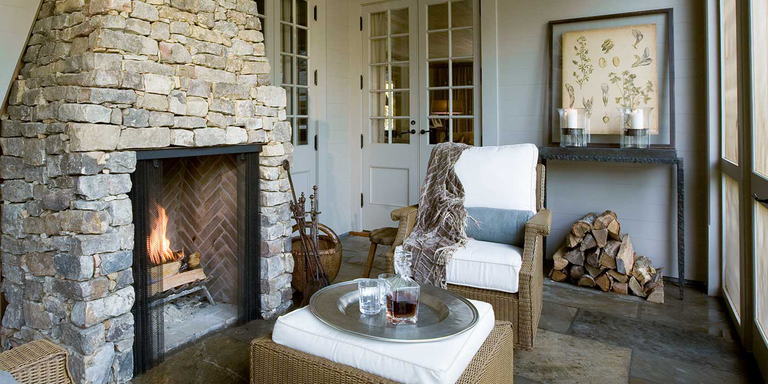 A rustic sunroom with a traditional, natural stone hearth and wood burning fireplace