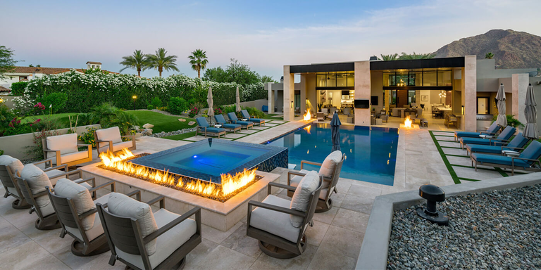 A luxury outdoor space with a pool, lounging area, and custom fire pit wall