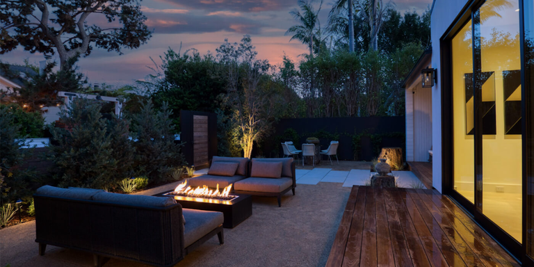 A modern luxury outdoor living space at nighttime with a lounge area and a lit linear gas fire pit