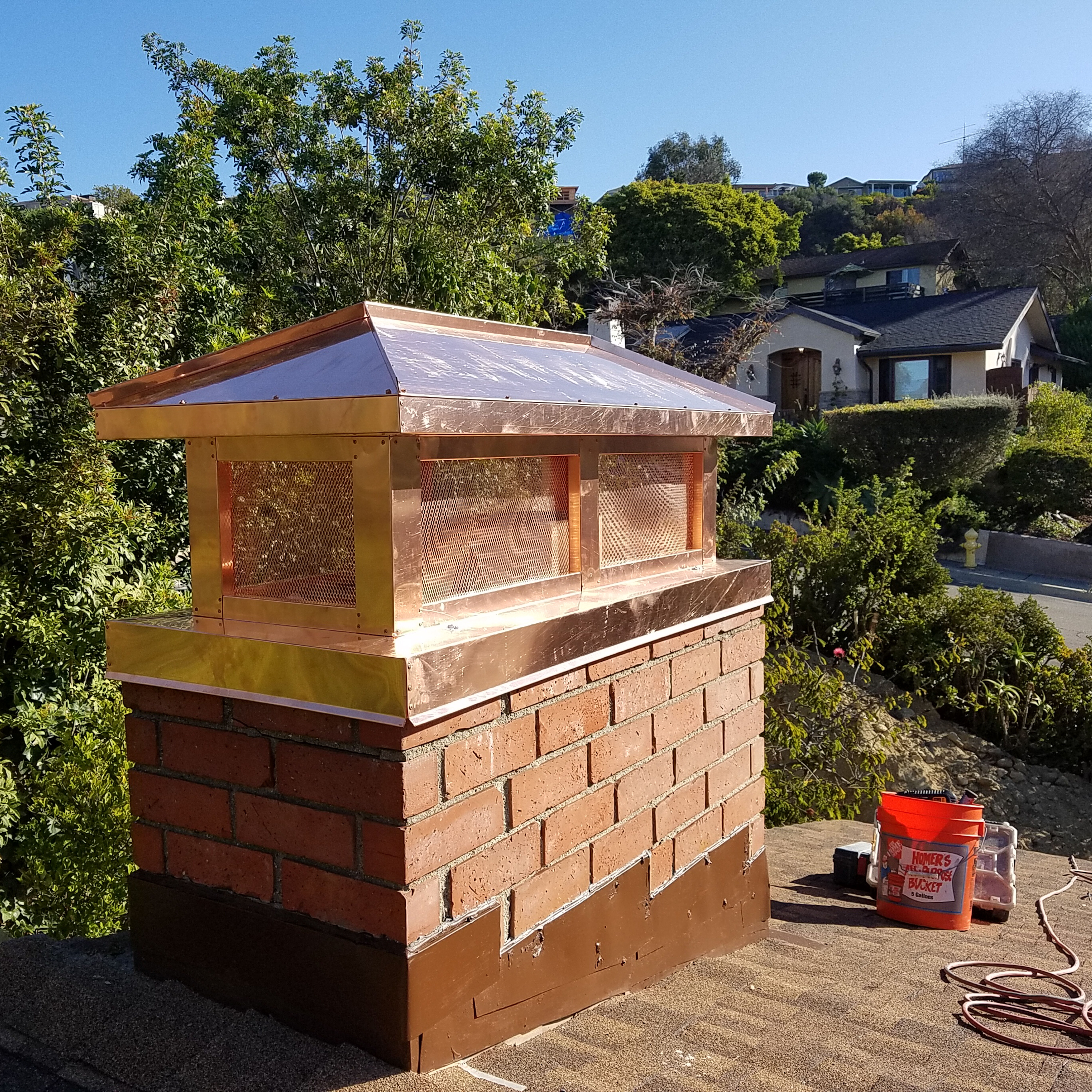 picture of a masonry chimney, a copper chimney cap, step flashing, and a roof, along with some chimney maintenance products