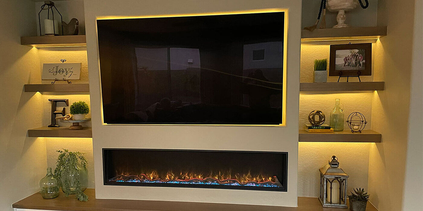 A custom-built electric fireplace feature wall with shelving, a TV, and LED uplighting under each shelf to showcase the decor